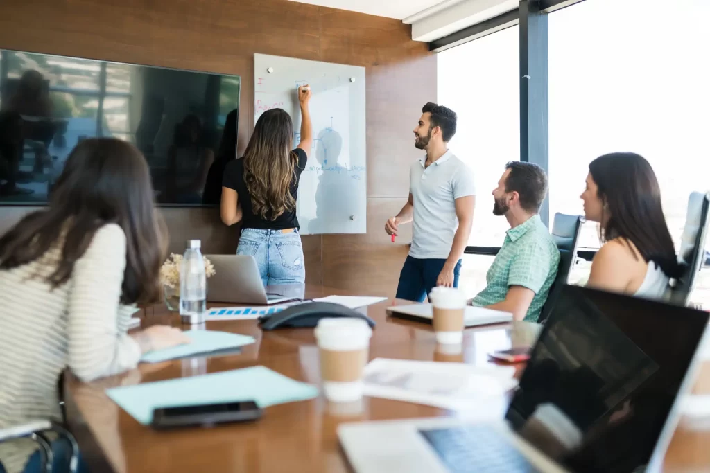 Formation FORMATEUR PROFESSIONNEL POUR ADULTES en Distanciel 1 collegues regardant femme affaires ecrivant tableau blanc au bureau pendant presentation scaled 1